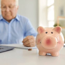Retired man at a desk with a pink piggy bank